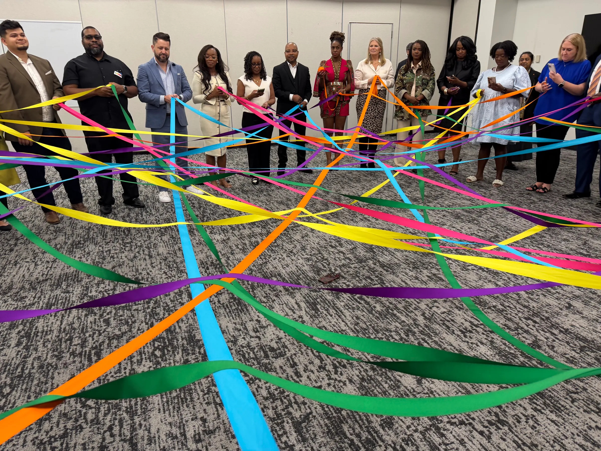 Business owners from the Goldman Sachs 10,000 Small Businesses cohort standing in a circle, holding a web of brightly colored ribbons stretched across the room between them.