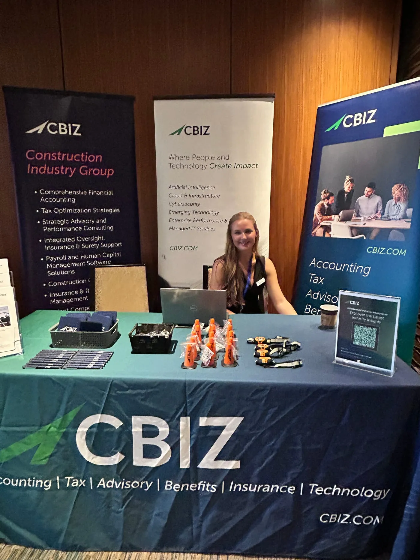 A staffed sponsor table at a construction financial management conference, with pull-up banners, giveaways and a laptop set up for conversations with attendees.